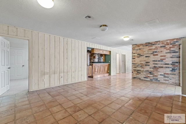 interior space with visible vents, a textured ceiling, brick wall, and wooden walls