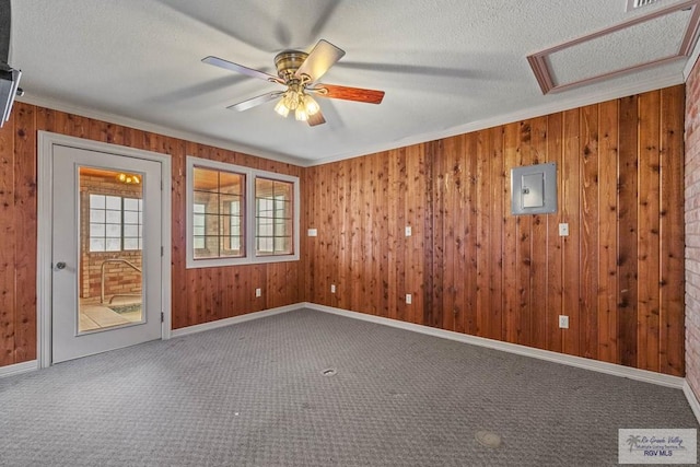 spare room featuring carpet flooring, wooden walls, electric panel, and attic access