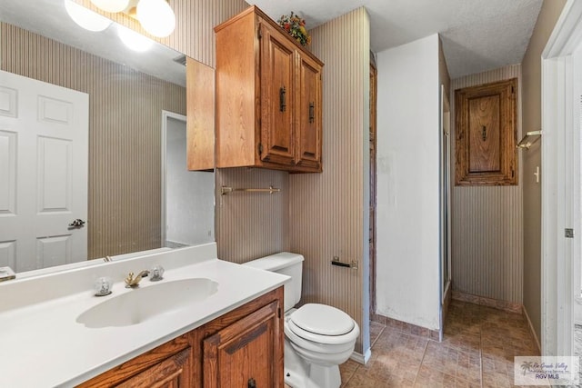 bathroom with toilet, wallpapered walls, baseboards, and vanity