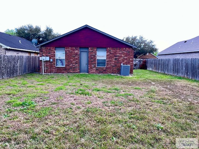 rear view of property with brick siding, a fenced backyard, central AC, and a yard