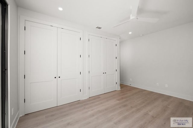 unfurnished bedroom featuring ceiling fan, light wood-type flooring, and two closets