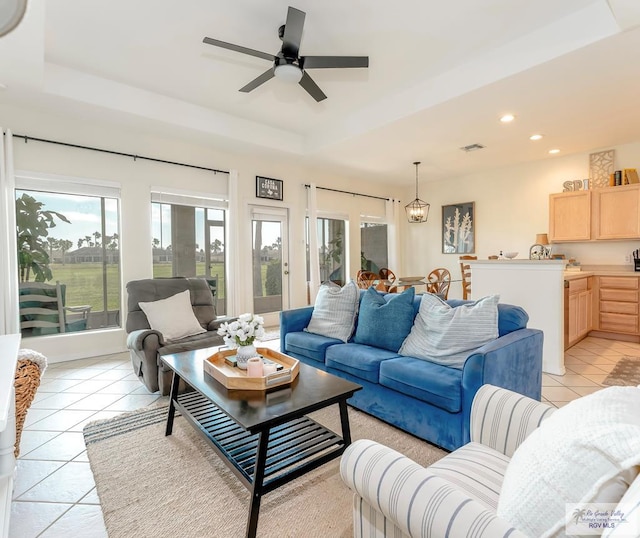 living room featuring ceiling fan with notable chandelier, light tile patterned floors, and a tray ceiling