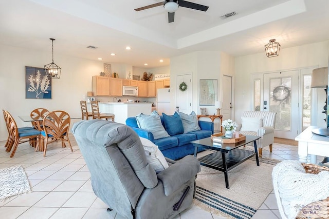 tiled living room featuring ceiling fan with notable chandelier, a tray ceiling, and sink