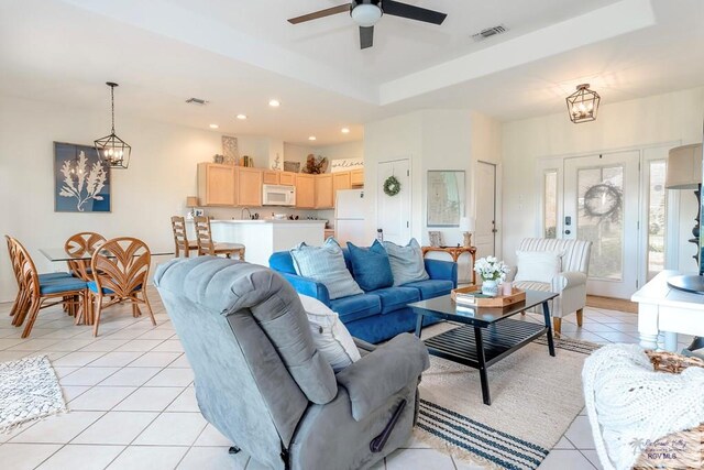 tiled living room featuring ceiling fan with notable chandelier, a tray ceiling, and sink