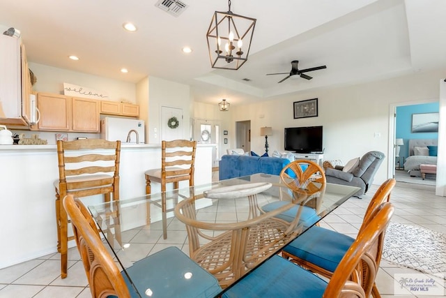 dining room featuring ceiling fan with notable chandelier, a tray ceiling, and light tile patterned flooring