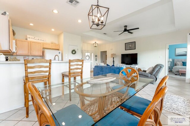 dining room featuring ceiling fan with notable chandelier, a tray ceiling, and light tile patterned flooring