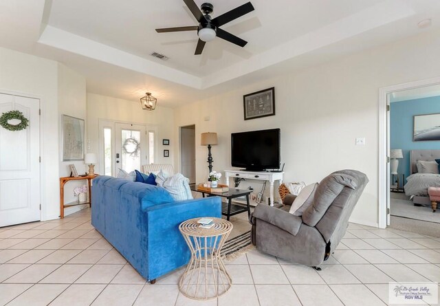 living room featuring light tile patterned floors, ceiling fan with notable chandelier, and a raised ceiling