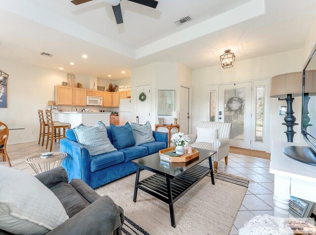 tiled living room featuring ceiling fan with notable chandelier and a raised ceiling