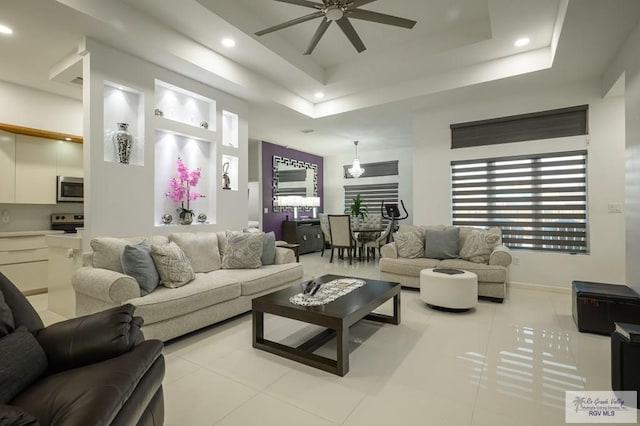 living room featuring a raised ceiling, ceiling fan, and light tile patterned floors