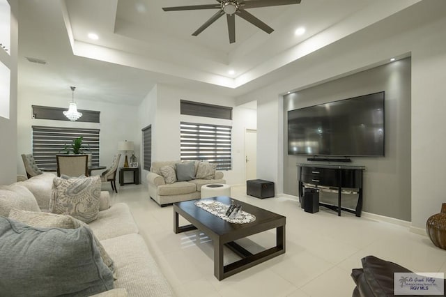 living room with a tray ceiling and ceiling fan with notable chandelier