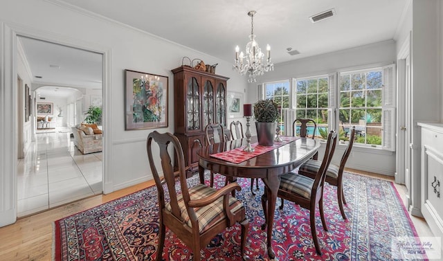 2301 Riverside Dr, Harlingen, TX 78550 - dining room featuring light wood finished floors, visible vents, arched walkways, crown molding, and a notable chandelier