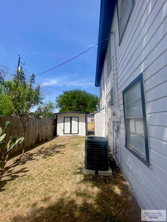 view of yard featuring central air condition unit, fence, an outbuilding, and a storage shed