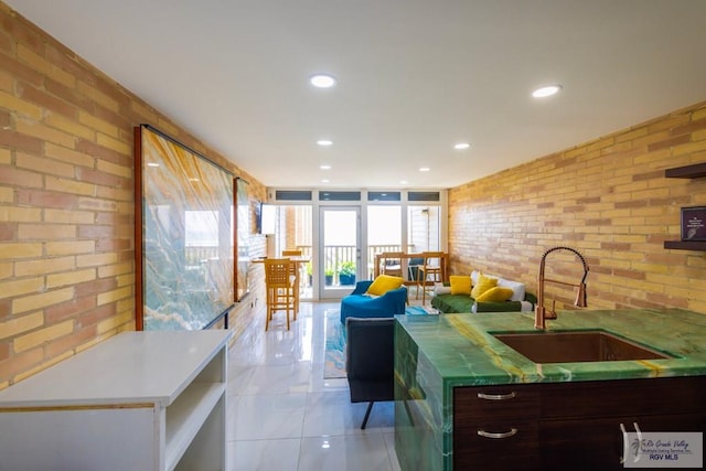 kitchen with light tile patterned floors, dark brown cabinetry, sink, and brick wall