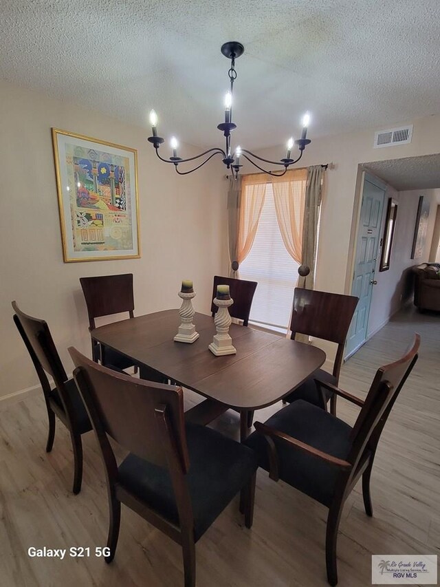 dining area featuring a notable chandelier, light hardwood / wood-style floors, and a textured ceiling