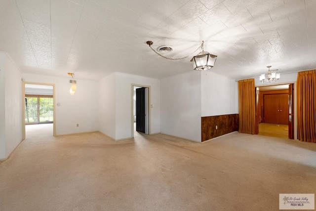 unfurnished room featuring carpet floors, wooden walls, and a notable chandelier