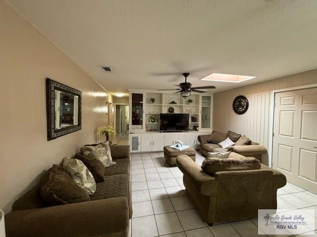 living area featuring light tile patterned floors, visible vents, a skylight, and a ceiling fan