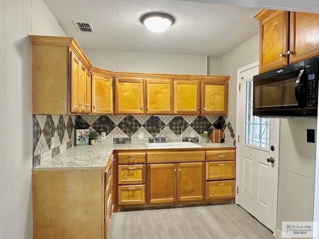 kitchen featuring backsplash, sink, a textured ceiling, and light hardwood / wood-style floors