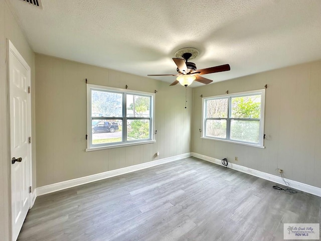 empty room with ceiling fan, a healthy amount of sunlight, wood-type flooring, and a textured ceiling