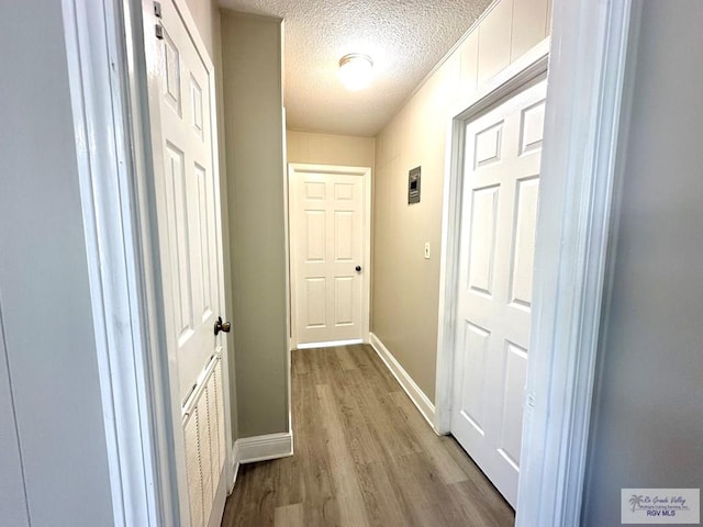 corridor with light wood-type flooring and a textured ceiling