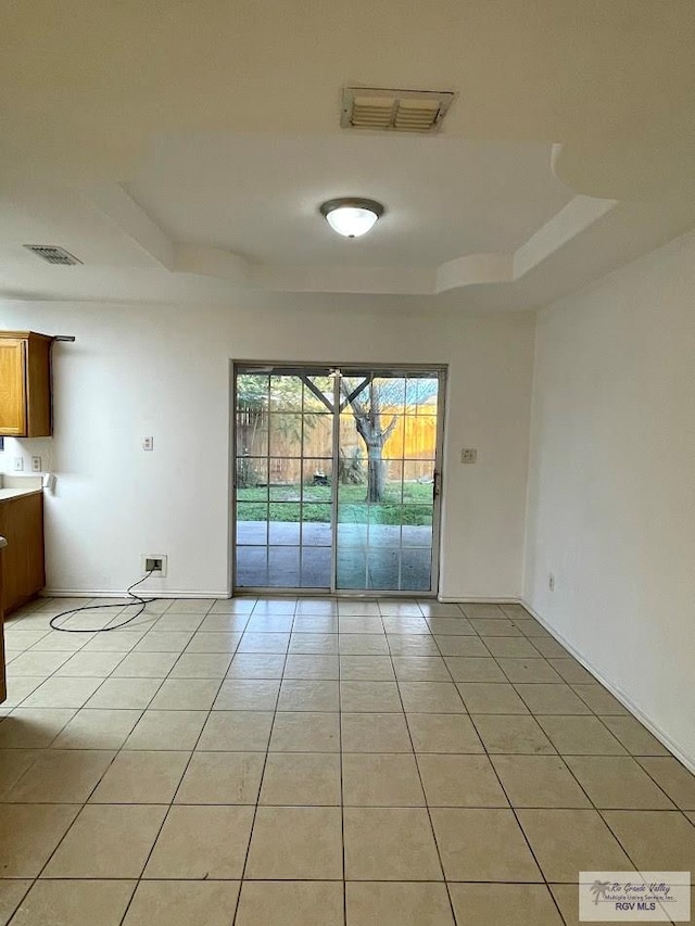 tiled empty room featuring a tray ceiling