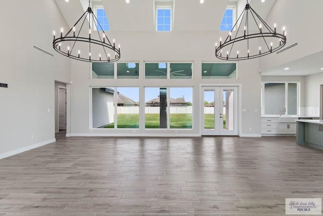 unfurnished living room featuring light wood-style flooring, a sink, a notable chandelier, and baseboards