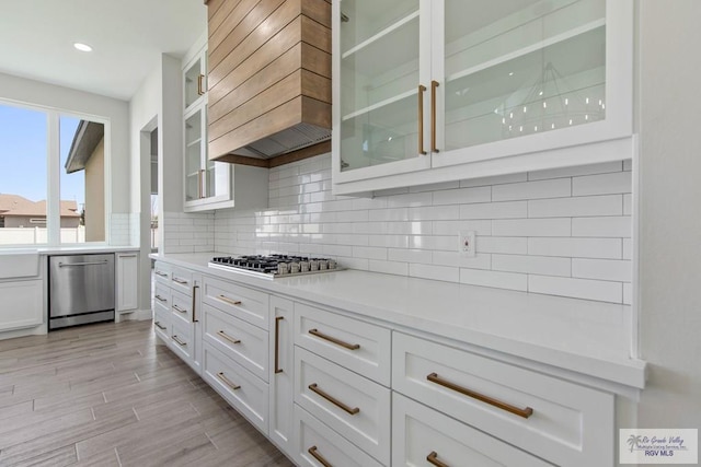 kitchen with light countertops, light wood-type flooring, backsplash, appliances with stainless steel finishes, and custom exhaust hood
