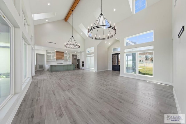 unfurnished living room with a chandelier, recessed lighting, beamed ceiling, and light wood finished floors