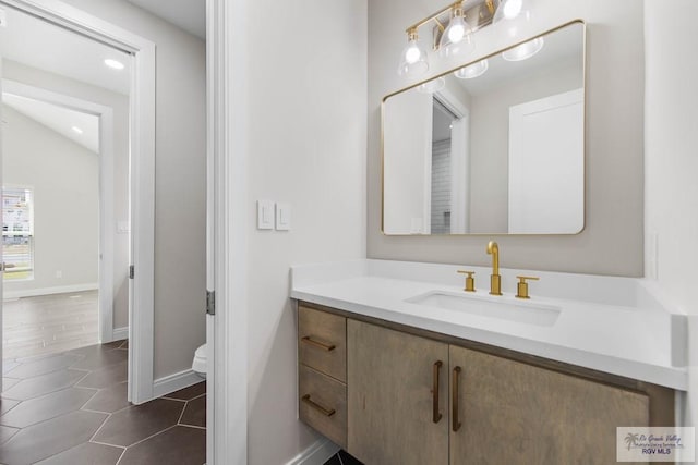 bathroom with baseboards, toilet, tile patterned floors, vanity, and lofted ceiling