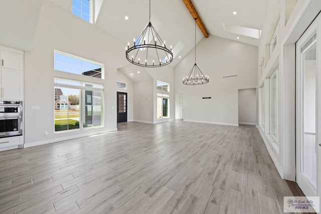 unfurnished living room featuring baseboards, light wood-style floors, a notable chandelier, and beam ceiling