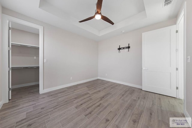 unfurnished bedroom with visible vents, wood finished floors, a walk in closet, and a raised ceiling