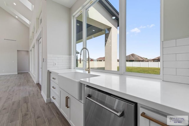 kitchen featuring light countertops, a sink, white cabinetry, wood finished floors, and stainless steel dishwasher