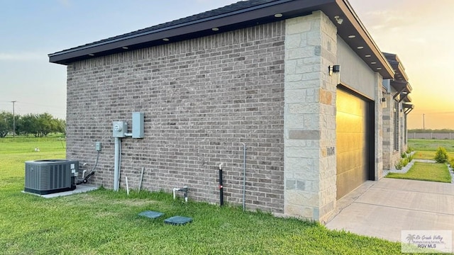 property exterior at dusk with a lawn, cooling unit, and a garage