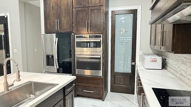 kitchen featuring decorative backsplash, custom exhaust hood, dark brown cabinetry, stainless steel appliances, and sink