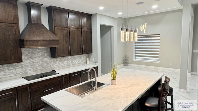 kitchen with black electric stovetop, custom range hood, sink, hanging light fixtures, and a breakfast bar area