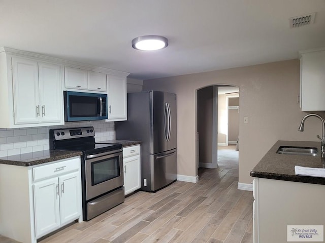 kitchen with tasteful backsplash, visible vents, arched walkways, appliances with stainless steel finishes, and a sink