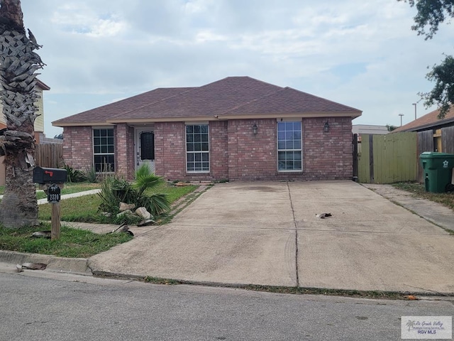 ranch-style house with brick siding, fence, and roof with shingles