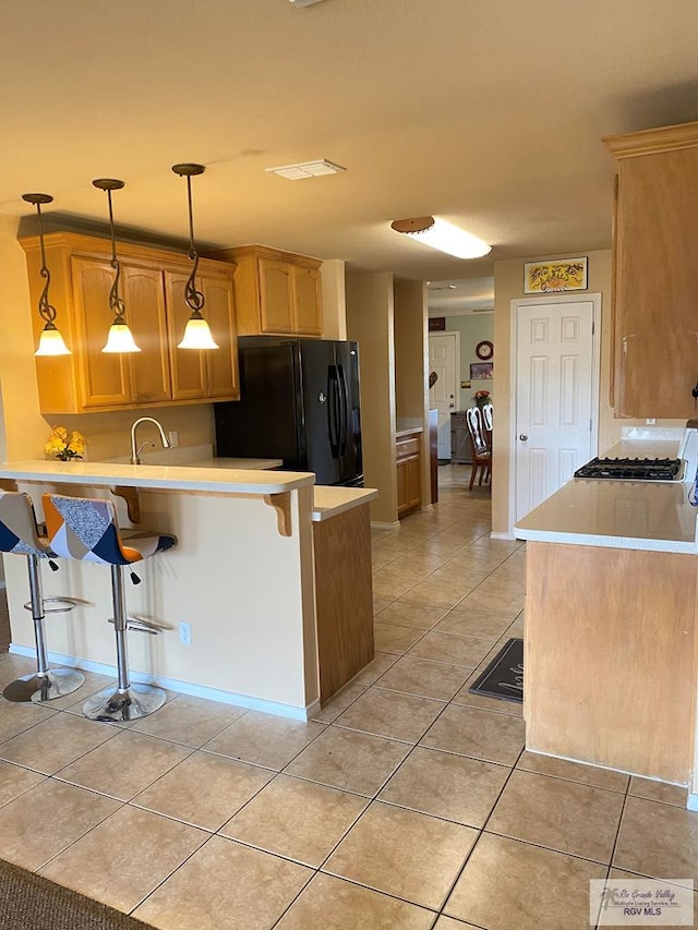 kitchen featuring pendant lighting, black fridge, light brown cabinets, kitchen peninsula, and a breakfast bar area