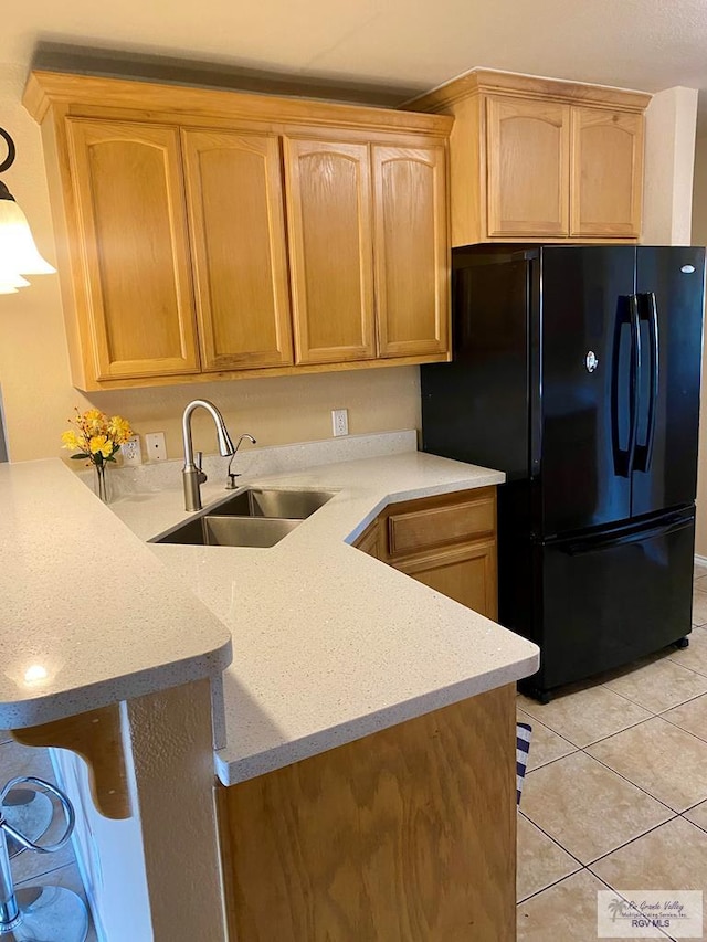 kitchen featuring light tile patterned floors, sink, black fridge, and kitchen peninsula