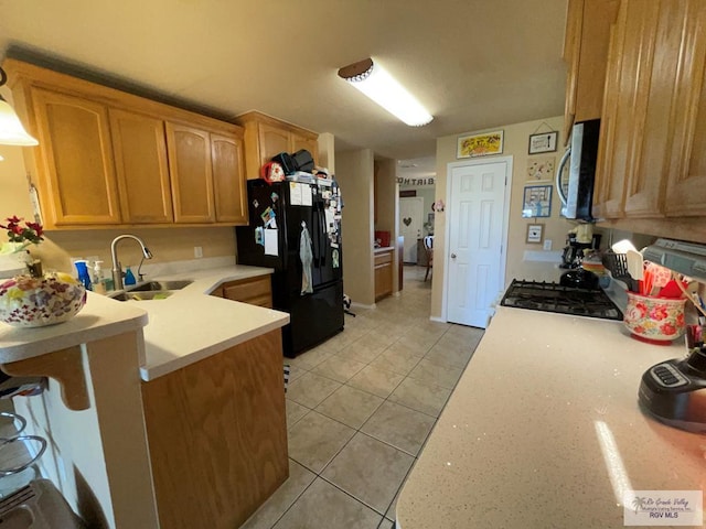 kitchen with black refrigerator, light tile patterned floors, sink, and stove