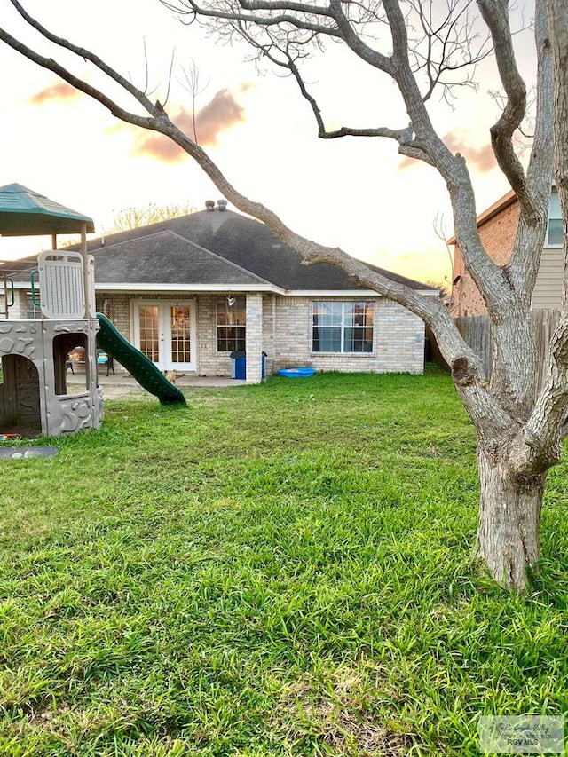 back house at dusk featuring a playground and a lawn