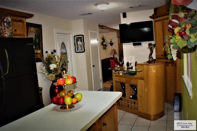 kitchen featuring black refrigerator, light tile patterned floors, and a textured ceiling