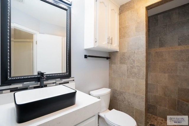 bathroom with tiled shower, tasteful backsplash, vanity, and toilet