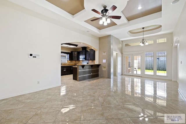 living room with coffered ceiling, ceiling fan with notable chandelier, a towering ceiling, and a tray ceiling