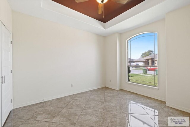 empty room featuring plenty of natural light, ceiling fan, and a raised ceiling