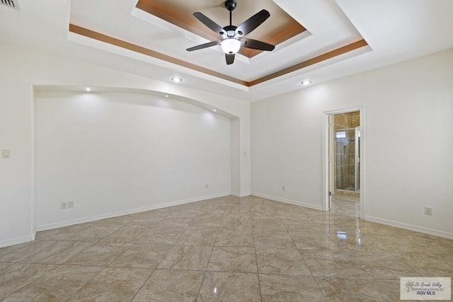 unfurnished room with ceiling fan and a raised ceiling