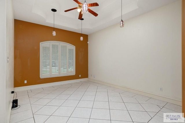 tiled empty room with ceiling fan and a raised ceiling