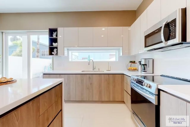 kitchen featuring a sink, light countertops, range with electric cooktop, stainless steel microwave, and modern cabinets