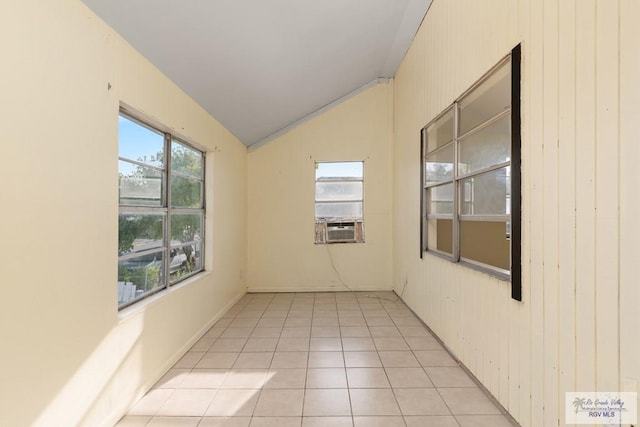 empty room featuring wooden walls, a wealth of natural light, lofted ceiling, and light tile patterned floors