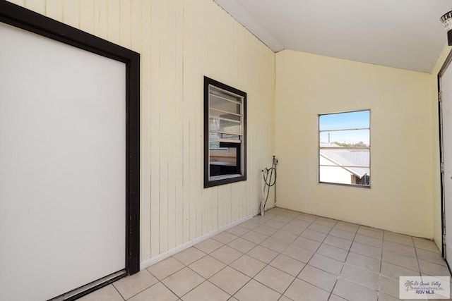 tiled empty room featuring wood walls and vaulted ceiling