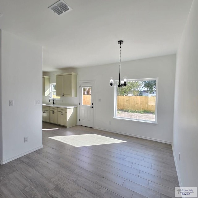 unfurnished dining area featuring a notable chandelier, sink, and light hardwood / wood-style flooring